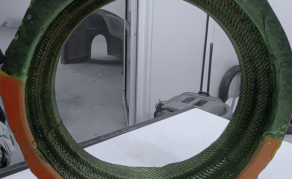 Carbon twill fabric stacked inside the orange-and-green two-piece composite rim mold, the weave visible around the full circumference