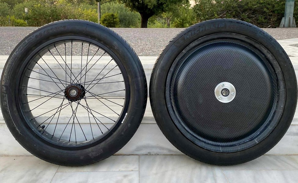 The old wire-spoked wheel with an inner tube standing beside the new single-piece tubeless carbon-fibre wheel, both tires fitted