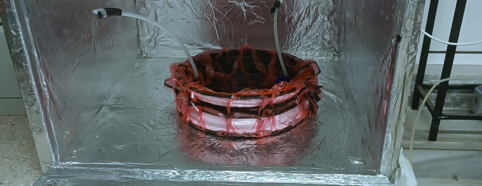 Inside the oven's foil-lined chamber: a carbon-fibre rim on a rack under red vacuum bagging, with two thermocouple leads run in through the chamber wall