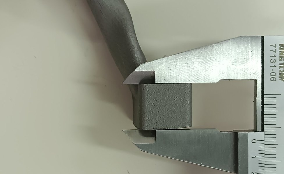 A vernier caliper closed on a square as-built boss of the printed motor mount, checking the scan result by hand