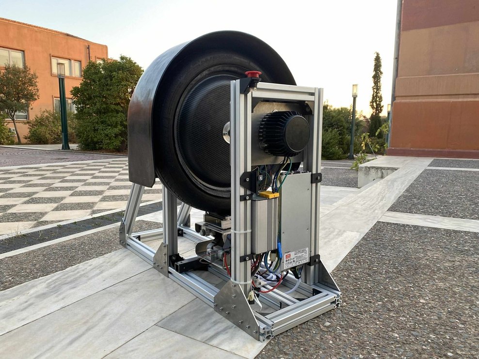 The instrumented wheel test bench: a wheel mounted on a driven shaft in a welded steel frame, with the loading arm, motor and wiring loom alongside